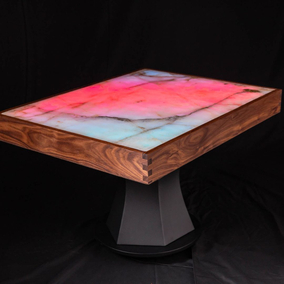 Modern table with a glowing, colorful surface and wooden frame on a black geometric base.