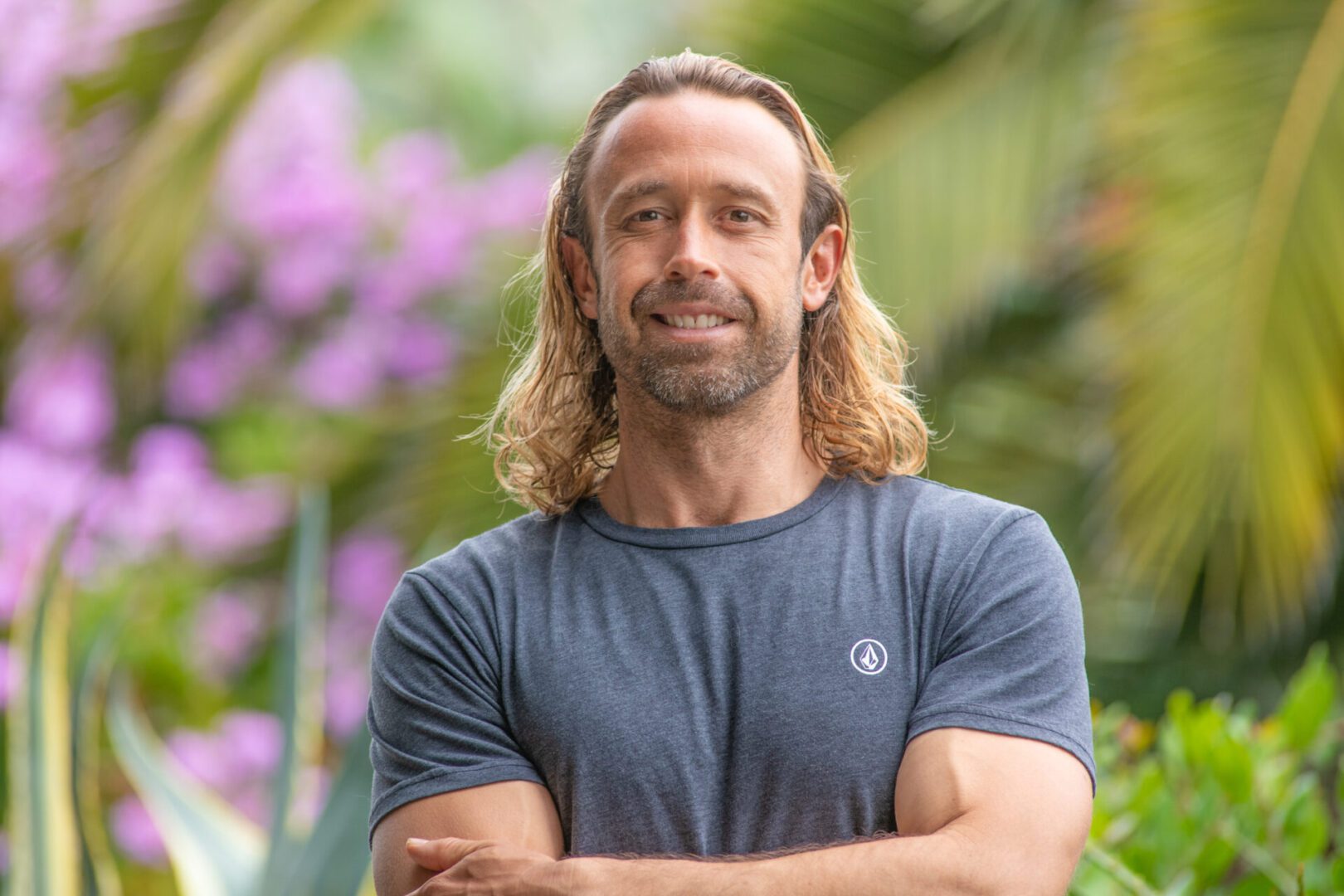 Smiling man with long hair and beard standing outdoors.