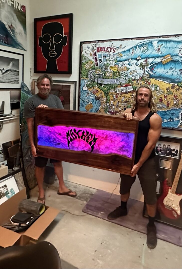 Two men holding a vibrant neon sign with artwork in a studio.