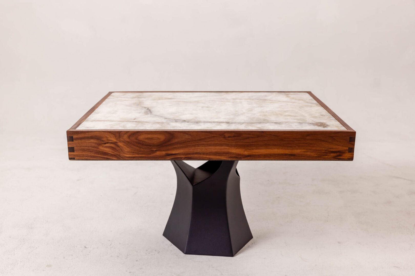Square marble-top table with wooden trim and black sculpted base.