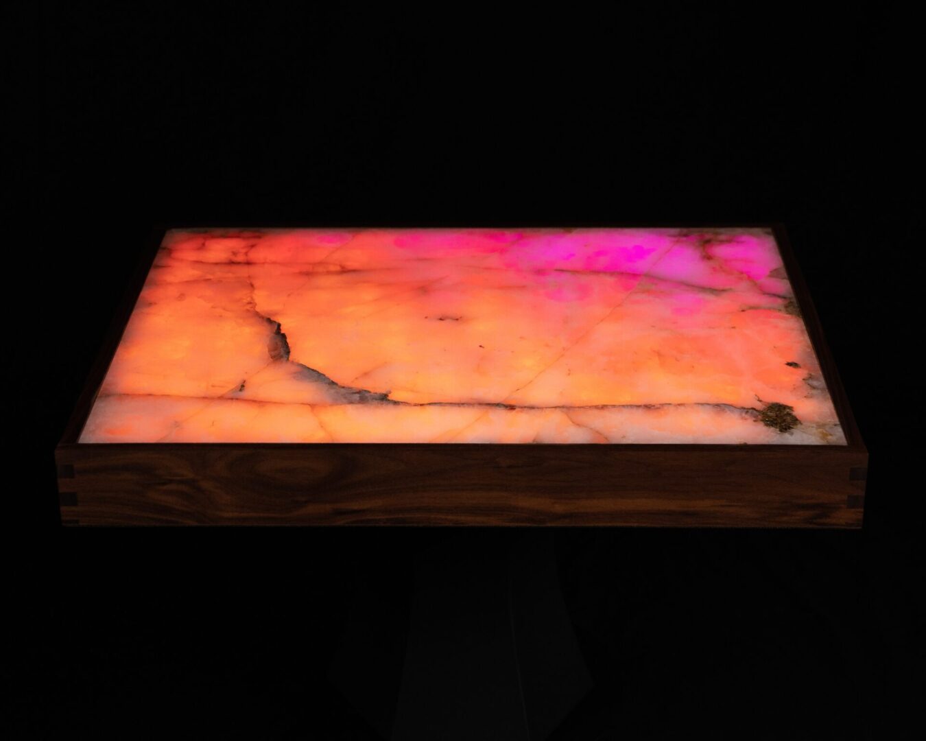 Illuminated rectangular stone slab with warm orange and pink hues on a dark background.
